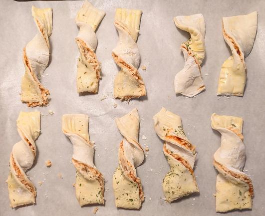 Image shows a sheet pan with 10 puff pastry pizza twists on it about to go in the oven.