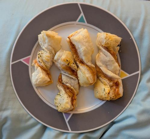 Image shows a grey and white plate with 4 fully baked puff pastry pizza twists on it.