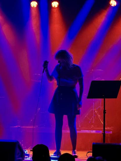 The singer of Frýs in silhouette with blue and red lights behind her