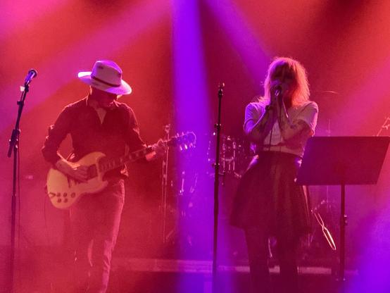 The guitarist and singer on stage with red lights bathing the scene and swath of purple light in the middle