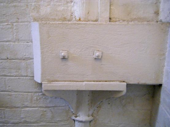 The bolts and other structural features of what I *think* is a pipe junction appear to form a sad face. It, and the wall behind it, are painted white. I saw this in a stairwell in the Barrows in Glasgow.
