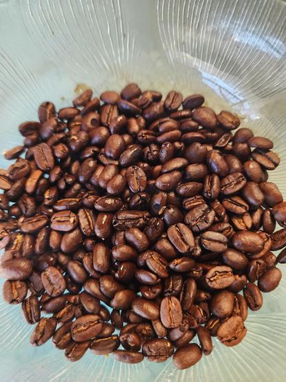 A small glass bowl full of chocolate brown, slightly glossy coffee beans.
