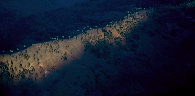 Early morning sunlight illuminates a mountain ridge, scattered with gum trees