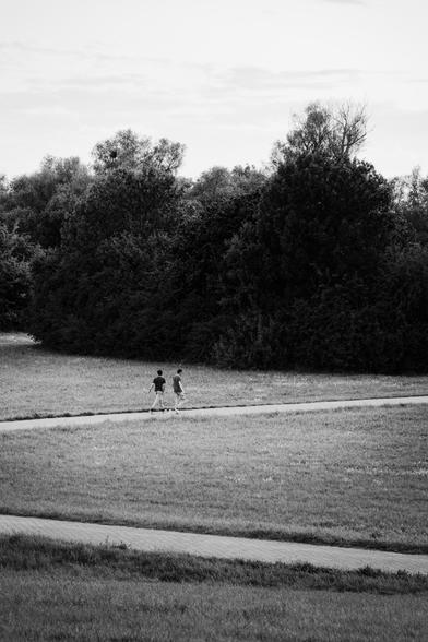 Two people walking on a path in front of big bushes and trees 