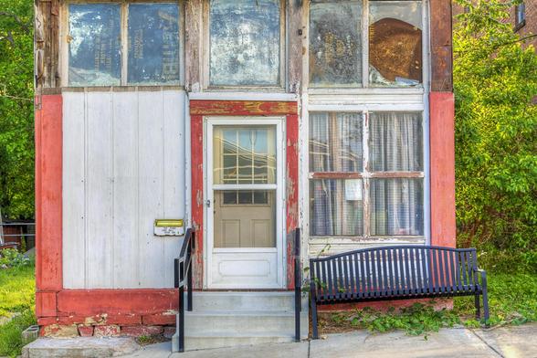 A weathered building facade features a central door flanked by two large windows, with peeling paint and visible signs of age. 