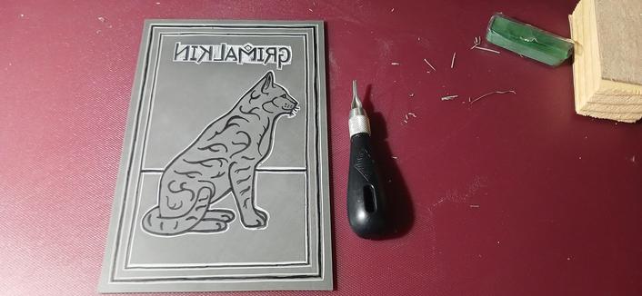 Image of my Grimalkin cat being cut into lino. The process is still unfinished. These photos show the overall design, the close up of the cat, still only outlined, and the text basically cut out in detail.