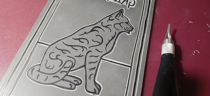 Image of my Grimalkin cat being cut into lino. The process is still unfinished. These photos show the overall design, the close up of the cat, still only outlined, and the text basically cut out in detail.