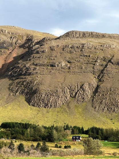 A tiny house at the base of a mountain with lots of greenery 