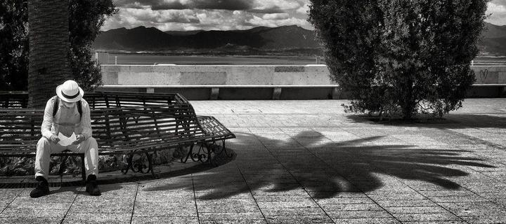 the reminder: a black-and-white photograph of a man sitting on a bench and reading a letter