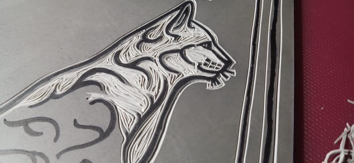 Image 2:

A closeup of my "Grimalkin" cat being carved into lino. There is an image of the cat drawn onto the lino with black permanent marker and deep grooves cut around the permanent marker design to create a raised image.