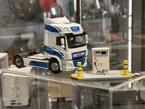 A miniature model of a battery-electric DAF tractor truck, next to a similarly small charging station with a green e-logo and yellow collision protection.