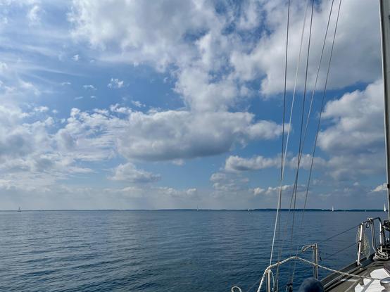Sønderborg Bugt. Glattes Meer an einem sonnigen Tag, Wolken mit viel Blau dazwischen. Am rechten unteren Rand ist ein Teil eines kleinen Segelbootes zu sehen.