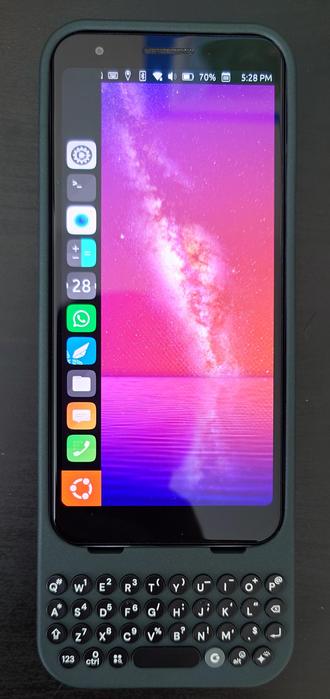 A Google Pixel 3a running Ubports 24.04-1.0 seated in a Clicks Keyboard case (normally for a Pixel 9) laying a black wood table.