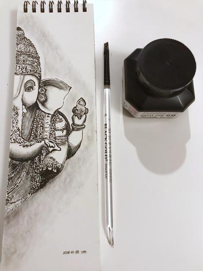 Black ink brushwork representing the other half of Ganesh on a talk and narrow drawing pad. The ink bottle and flat brush are at its side