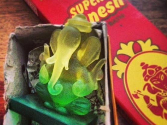À Chennai, Inde, une figurine verte/jaune de Ganesh posée dans une boîte grise, à côté se trouve de l'encens Super Ganesh. #NoVisa — La fête à Ganesh © 2022 Gilles Denizot