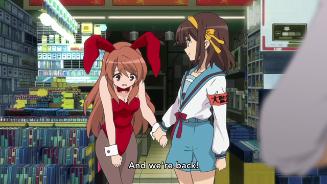A teenage girl (Haruhi) in a school uniform holding the hand of another teenage girl (Mikuru) who's in a red bunny girl costume appearing nervous while they stand in front of an open shop. A subtitle says, "And we're back!"