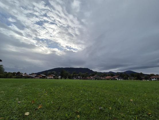 Green meadow with a line of houses in the distance. Some wood covered mountains in the background