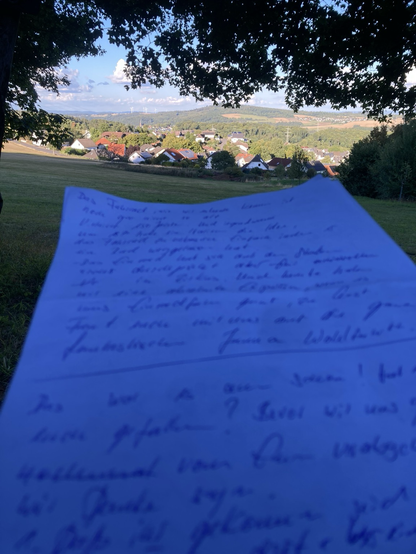 Im Hintergrund sieht man Hübingen in den Hügeln des Westerwaldes. Im Vordergrund ein Blatt Papier auf dem Stichpunkte für eine Varietémoderation stehen.