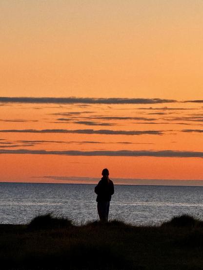 A person stares into a vivid sunset while standing on Skerjafjörður’s shore