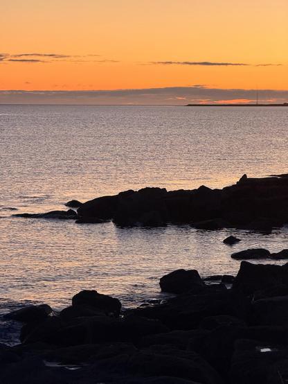 Rocks from Skerjafjörður can be seen in blue waters with a vivid sunset in the background 