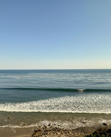 Picture of the Pacific Ocean taken from the southbound Amtrak Coast Startlight. Blue sky blue ocean with whitewash at the shore small wave breaking.