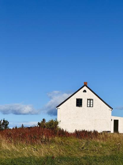 A stone house under a blue sky with puffy gray clouds in the distance and green and golden grasses in front