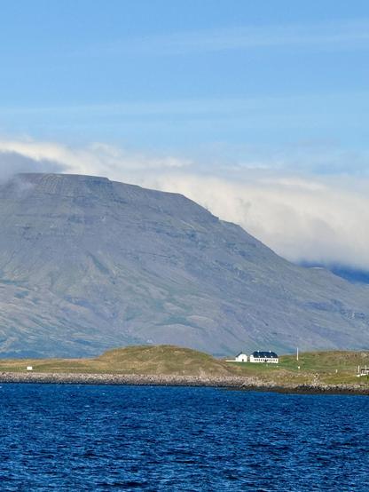 The island Viðey can be seen from across the harbor. The old house and church are in the foreground while Mount Esja is behind