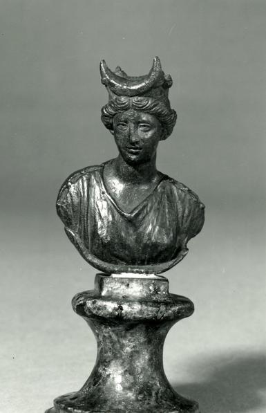 Cast bronze bust of the Roman moon-goddess Luna. She is wearing a chiton or peplos pinned over both shoulders and arms. A large lunar crescent adorns her head, reminiscient of horns.