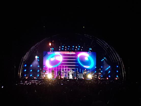 A view of the stage of an outside concert at night with coloured lights.