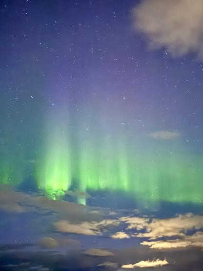 A line of purple and green aurora can be seen behind some clouds with the Big Dipper hovering above