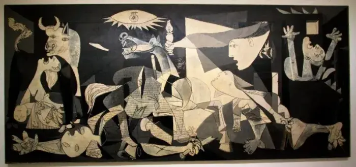 Picasso’s Guernica: a large black-and-white Cubist painting filled with distorted human and animal figures. A bull glares from the left, a horse screams at center, and fractured bodies—dead, dying, or reaching in agony—fill the canvas. An overhead bulb blazes down, evoking chaos and horror. The scene is a raw condemnation of violence and fascism.