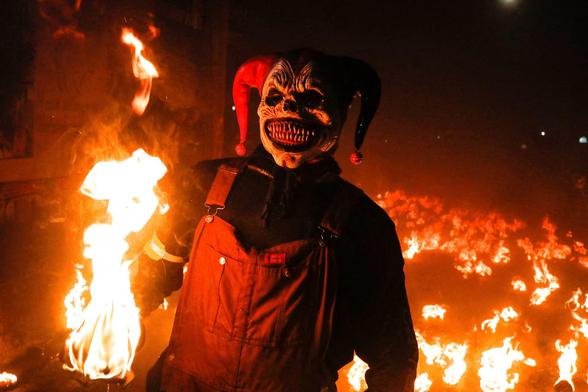 A man in a (devil's?) mask holds a ball of fire, with many more behind him.