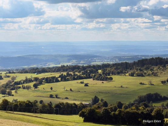 Weite Aussicht vom Hoherodskopf: sanfte Hügel und Wälder breiten sich bis zum Horizont aus, über ihnen ziehen helle Wolken, die dem Bild eine Atmosphäre von Freiheit und Fernweh verleihen.
