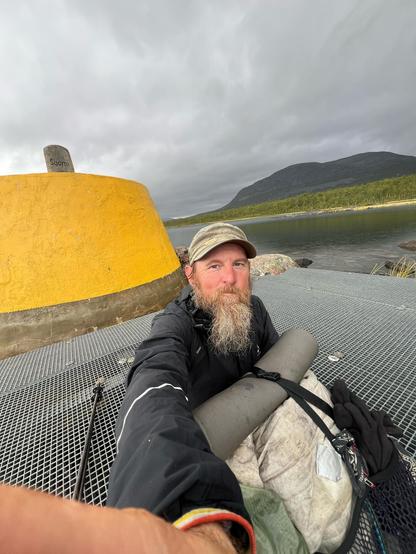 Yours truly with a long, grey, groom worthy beard, a white backpack in front of a large yellow cairn