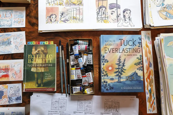 Sketches, watercolor paints, and copies of “Tuck Everlasting” by Natalie Babbitt and its graphic novel adaptation by K. Woodman-Maynard are arranged on a table
