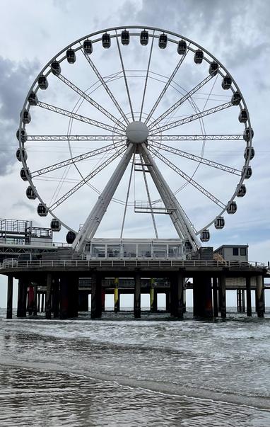 Ein ziemlich großes Riesenrad am Strand, aufgebaut auf einem Pier. Das Wetter ist merkwürdig- Sonne und Wolken. Es gibt dem Bild einen etwas morbiden Touch.
