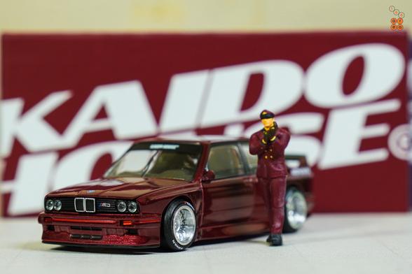 A BMW M3 E30, Kaido Works GT V1, Calypso Red Metallic by Mini GT in 1:64 scale with 1:64 figure on AREA 164