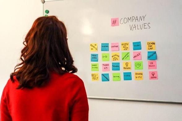 A woman looking at a whiteboard with post-it notes showing company values.