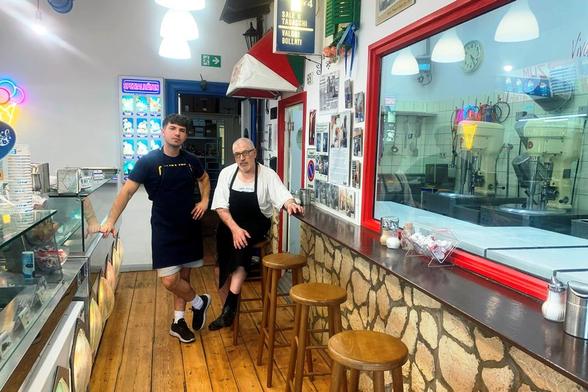 Luciano und Carlo Lanzano, Vater und Sohn, stehen in dem kleinen Gastraum ihrer Eisdiele zwischen dem Tresen und der hinter einem großen Fenster sichtbaren Küche.