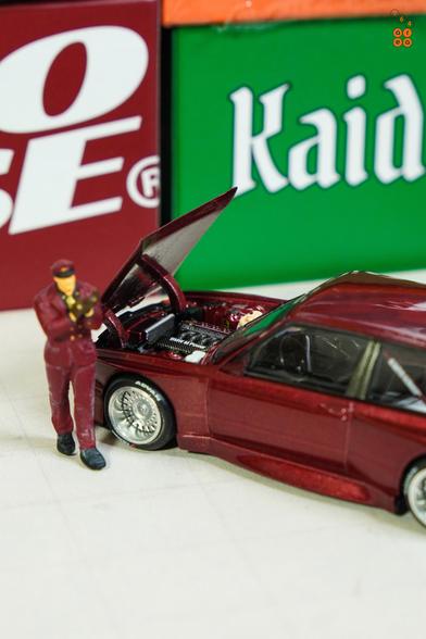 A BMW M3 E30, Kaido Works GT V1, Calypso Red Metallic by Mini GT in 1:64 scale with 1:64 figure on AREA 164