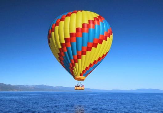 A bright colorful hot air balloon floating over the water with mountains in the distance