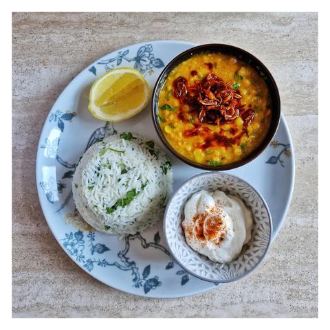 A plate with rice, dal some yogurt and a slice of lemon
