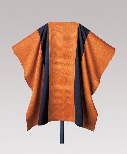 Túnica similar a un poncho. Es naranja con dos franjas oscuras verticales.