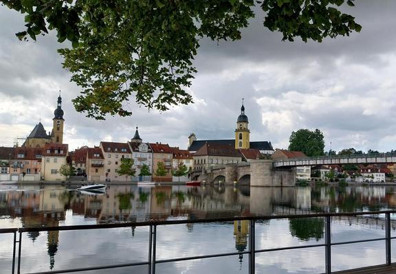 Stadtsilhouette hinter Fluss unter bedeckten Himmel und hereinragendem Laubbaum