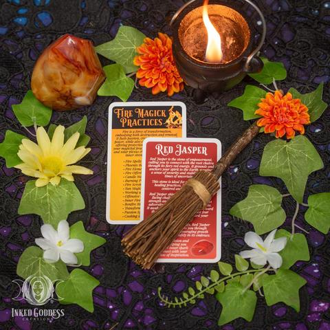 A set of 2 cards are arranged on a lace-covered tabletop. Each card in the "Phoenix Rising Eclectic Witch Card Expansion Pack" features information on aspects of fire and rebirth magick you can try, including info on the uses of Red Jasper in your renewal workings. This is an exclusive product from Inked Goddess Creations.