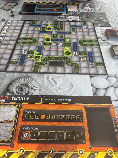 Das Spielbrett des Spiels, das einer Fabrik von oben nachempfunden ist. Vorne und hinten unsere Spielertableaus mit einer Checkpoint- und Energieanzeige und verschiedenen „Registern“ für Upgrade- und Programmkarten.