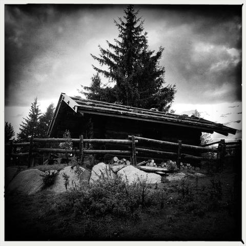 Una malga in legno circondata da uno steccato sopra ad una collina con dei grandi sassi