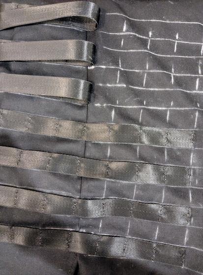 Black webbing being sewn onto black pants.