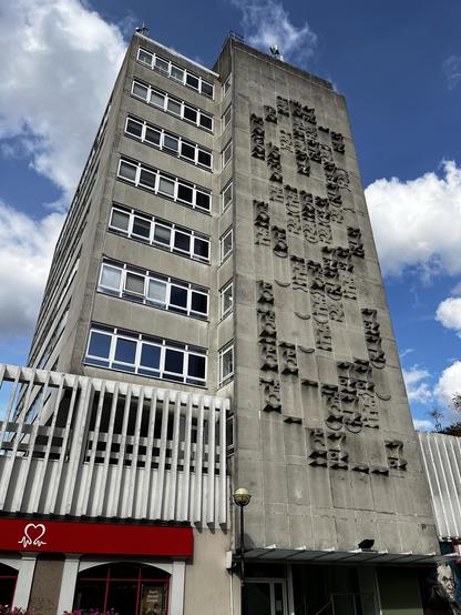 Ground-level shot of a mid-height concrete building, featuring a relief sculpture on the side.