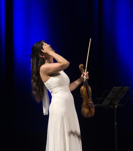 Lia en robe blanche, son violon à la main, l'autre main sur son front la tête renversée vers l'arrière, riant